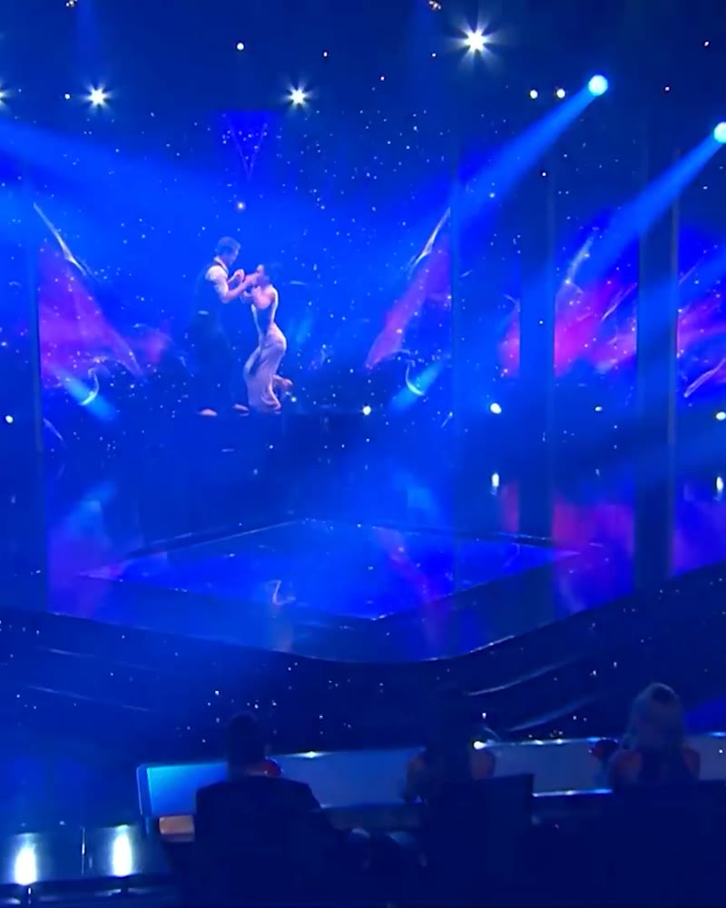 Two performers in a hand-to-hand lift on a dark starry stage