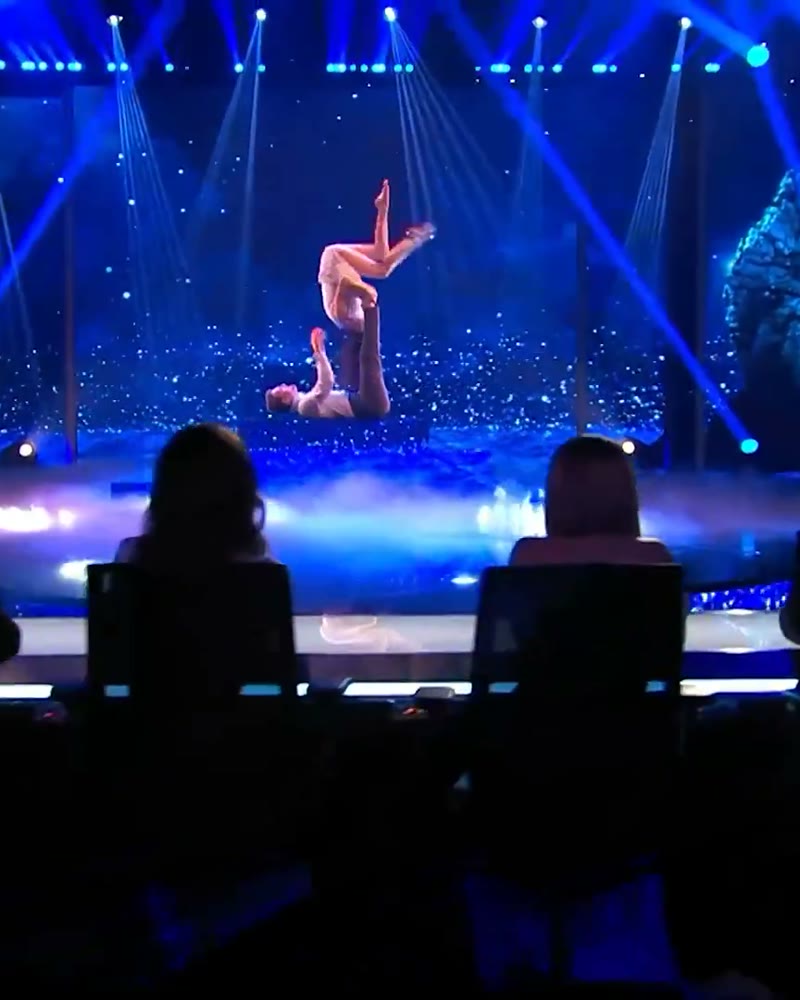 Two performers in a partner acrobatics lift on a blue stage
