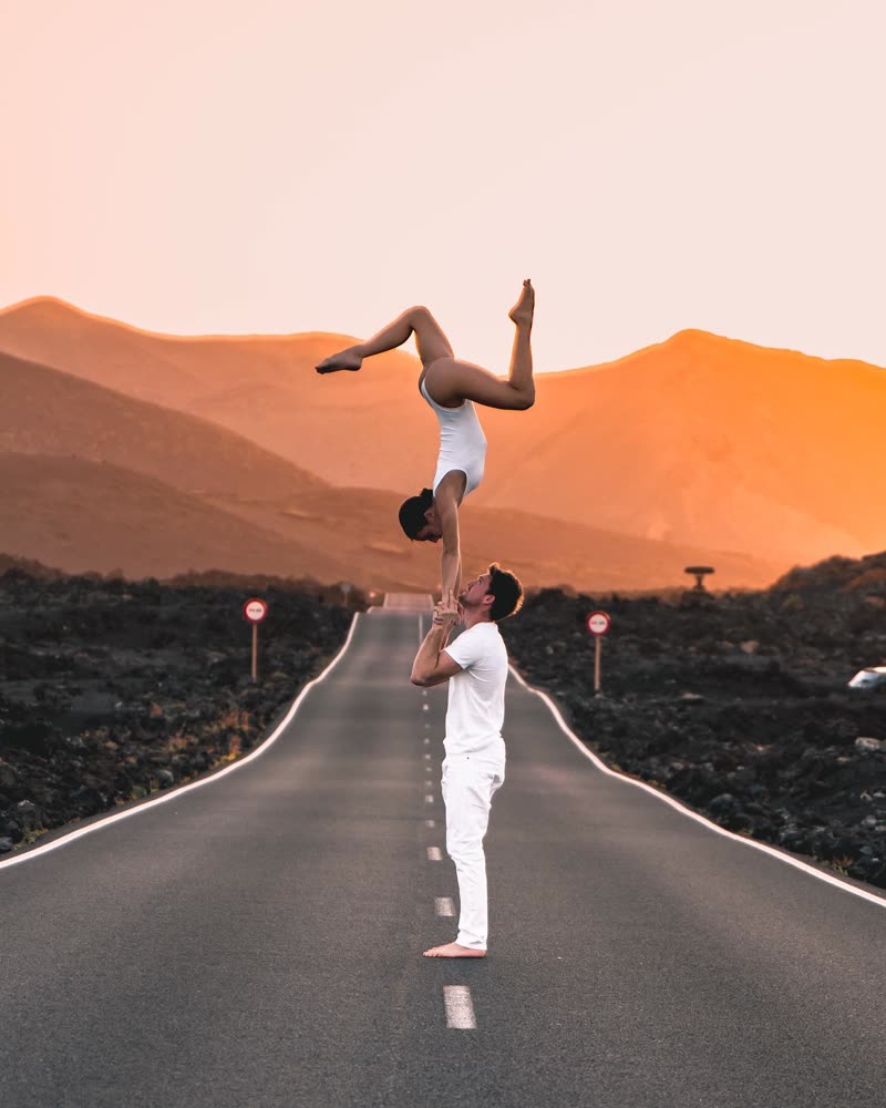 Handstand on the partner's shoulders on an empty road with orange mountains at sunset