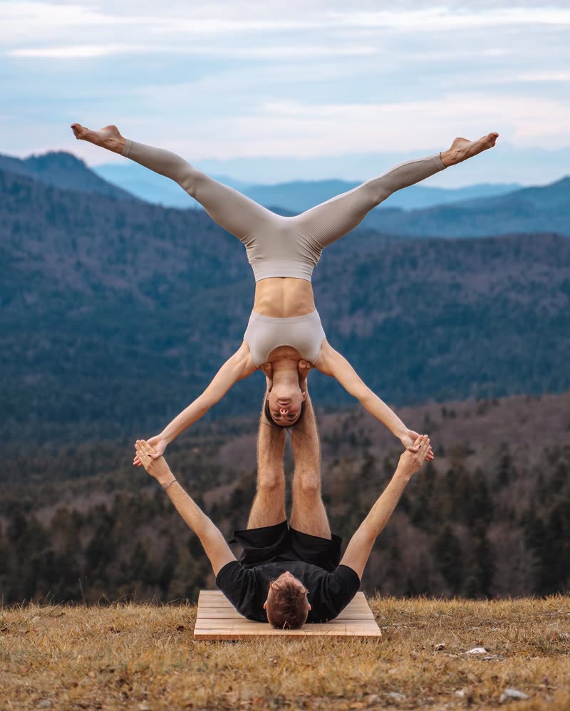 Inverted split above a partner lying on a wooden platform on a mountain meadow