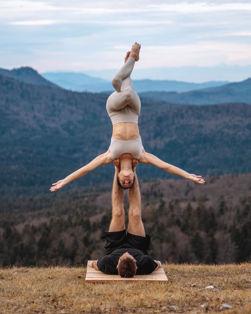 Inverted balance with arms stretched wide above the base partner on a mountain meadow