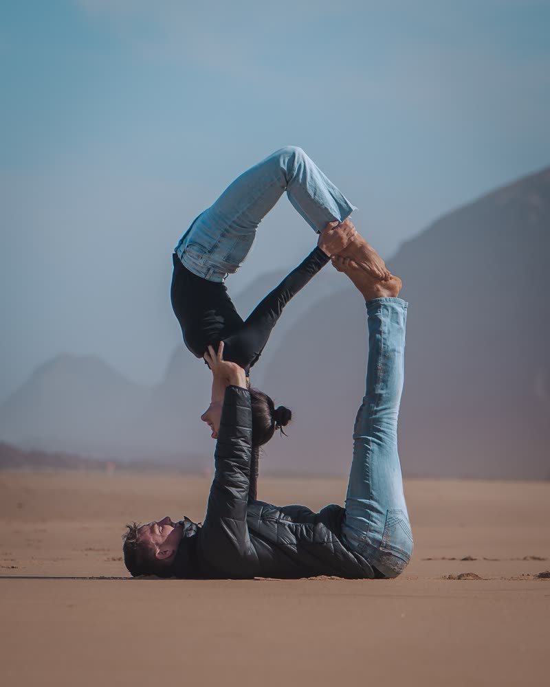 Partner acrobatics on a sandy beach with misty mountains in the background