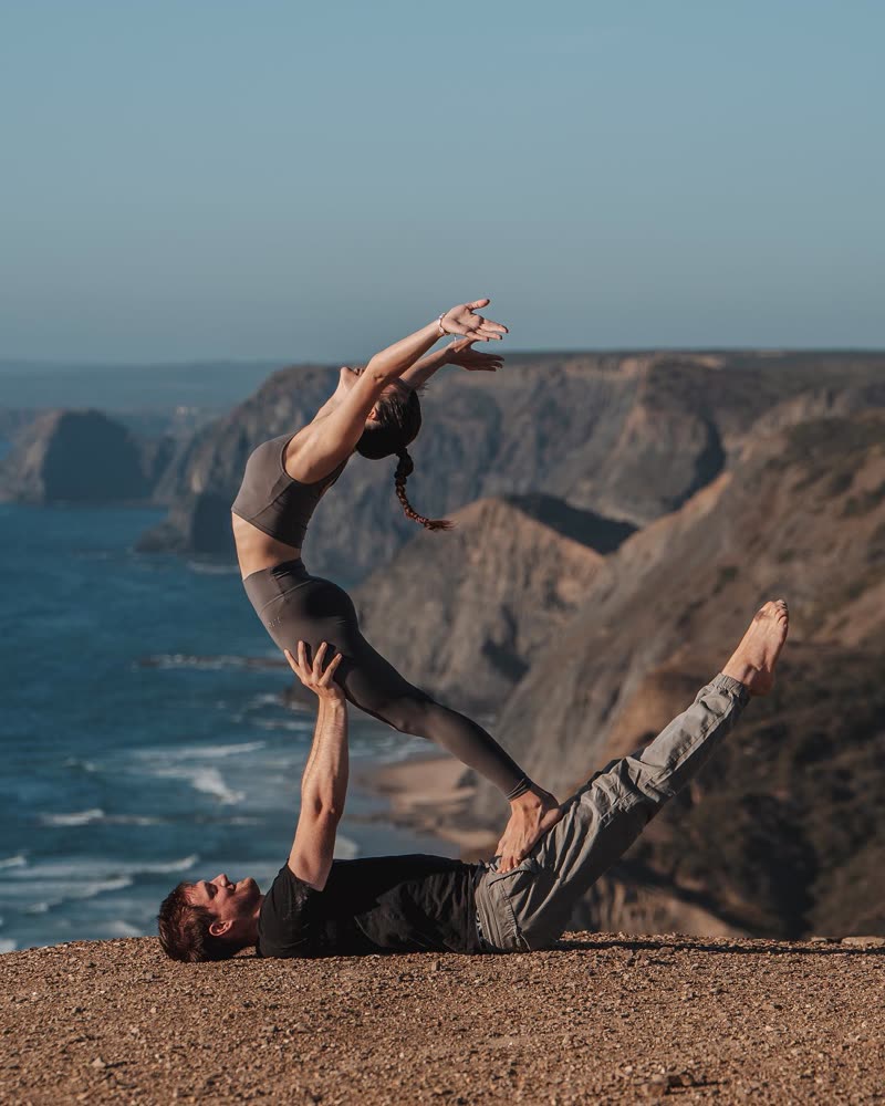 Elegant back-bend balance above a partner lying on a cliff by the ocean