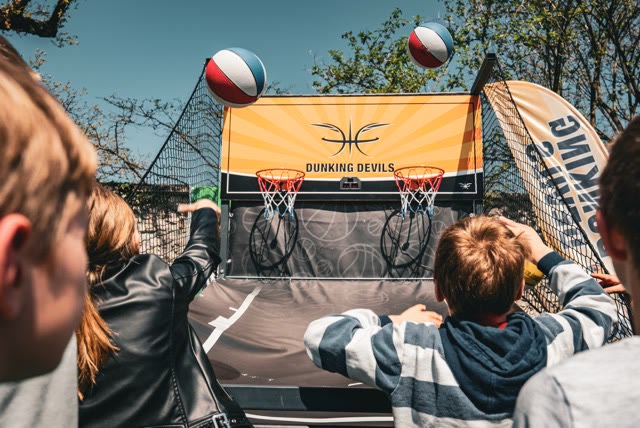 Children playing the arcade basketball game with two hoops and a Dunking Devils backboard, two balls in the air