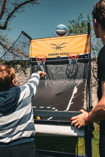 Boy reaching to shoot a ball at the arcade basketball game while a coach stands beside it