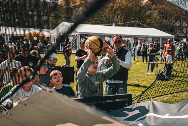 Boy in the crowd taking a shot at the arcade hoop while spectators watch