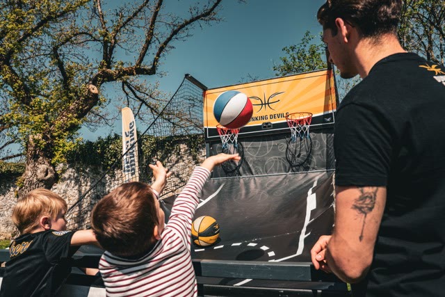 Child reaching for a ball at the arcade basketball game with a coach watching