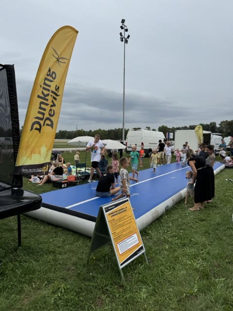 Children of different ages on the air track with a Dunking Devils flag and a trampoline beside it
