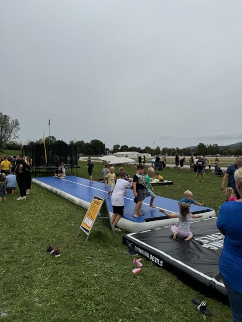 Children on the air track and a nearby landing mat at a family event in a field
