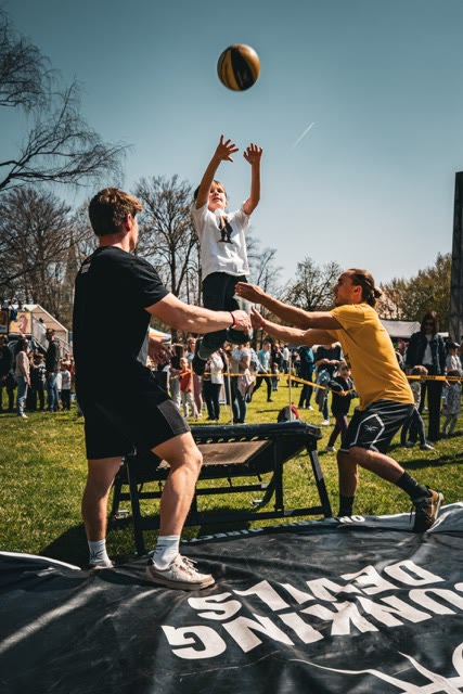 Child in mid-air throwing the ball above a mini trampoline between two coaches
