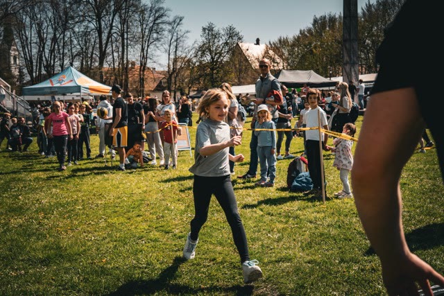 Girl running towards the activity area at the outdoor basketball workshop while other children wait