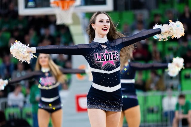 Dancer with pom-poms and arms stretched wide in a sparkling navy costume