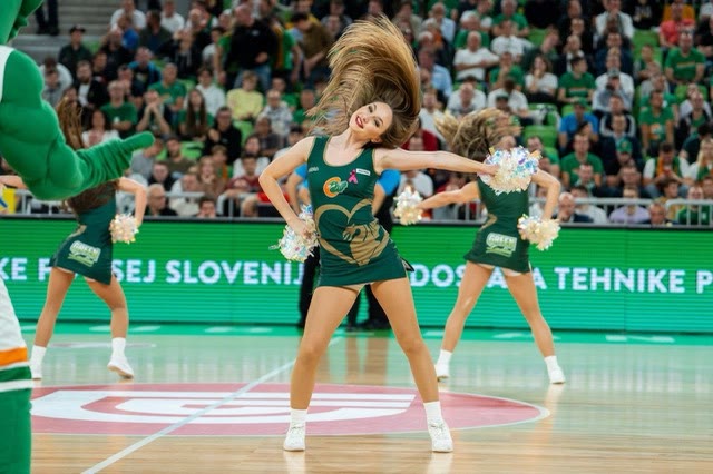 Dancer in a green costume with flying hair and pom-poms in front of the audience