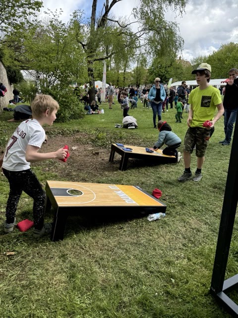 Children and teenagers playing cornhole on two boards at an outdoor event