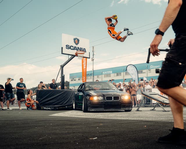 Athlete dunking over a parked car in front of a crowd at an outdoor event