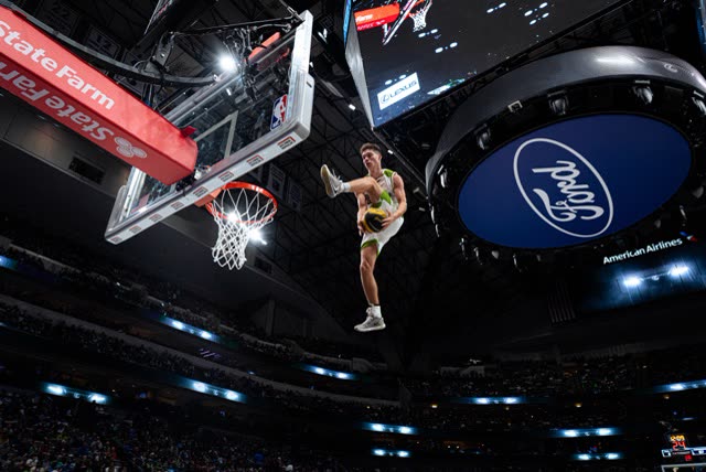 Close-up of an athlete in mid-air holding the ball beside the hoop in an NBA arena