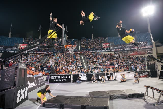 Three athletes flipping and dunking at a FIBA 3x3 World Tour event in front of a full stand