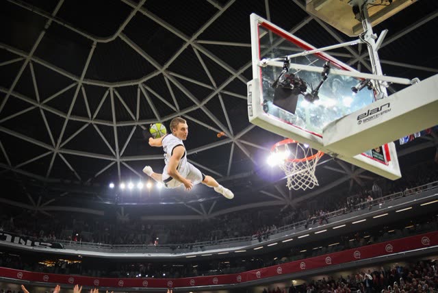 Athlete in white soaring towards the hoop beneath the roof of a large indoor arena