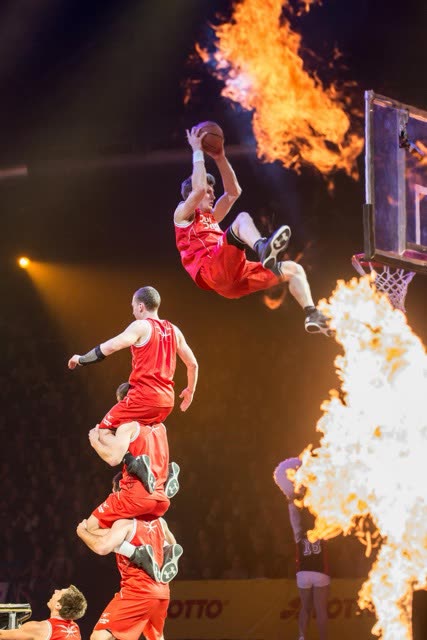 Athlete dunking above a human tower between two tall flames in a dark arena