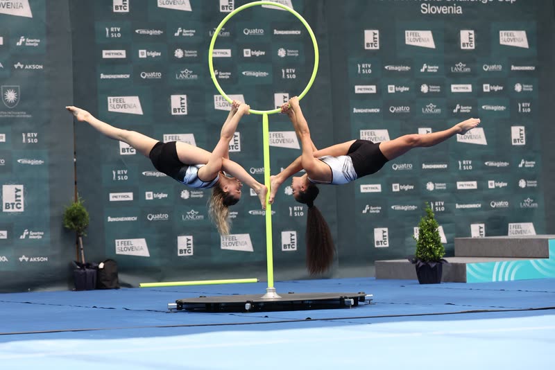 Two aerialists in synchronized split poses on a freestanding aerial hoop at a competition