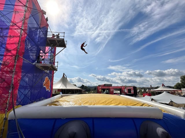 Jumper falling backwards towards a large yellow and blue airbag from a tall tower at a festival
