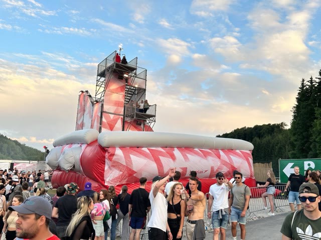 Tall jump tower with a staircase behind a large red and white airbag with spectators in front at sunset