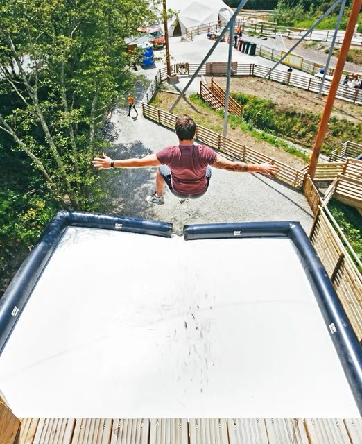View from the top of a jump platform as a participant leaps with arms out towards a white airbag
