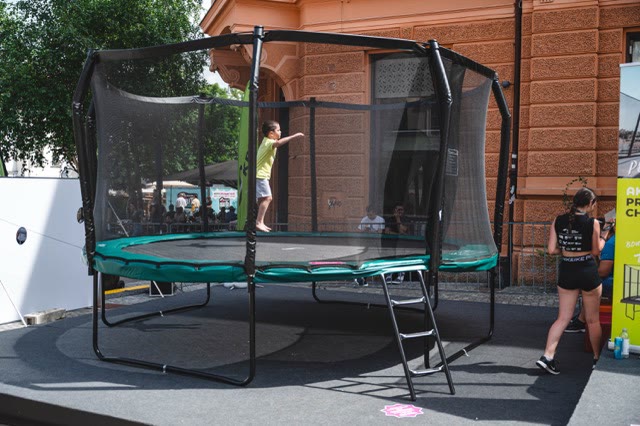Child bouncing on a large round garden trampoline with a safety net and ladder on an event stage