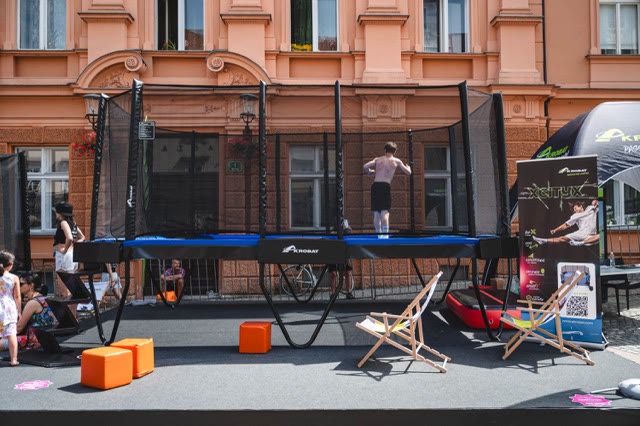 Rectangular trampoline with a safety net, orange seat cubes and deck chairs on a stage in a city street