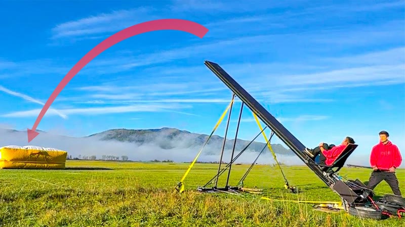 Flyer on the human catapult ramp with a yellow landing airbag in the distance in a green field