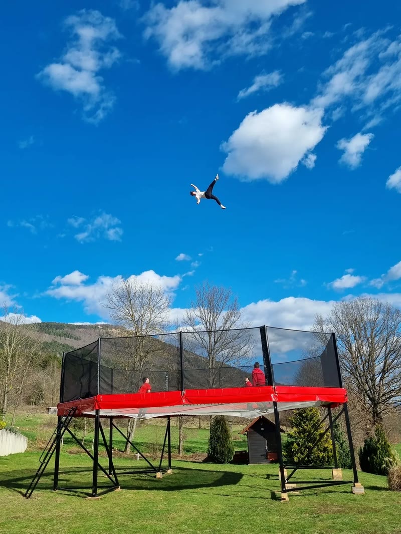 Acrobat flying high in the air above the red Megatramp against a deep blue sky