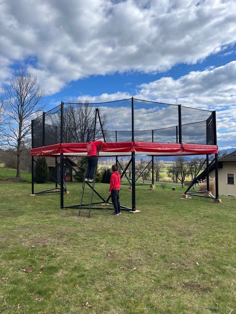 The Megatramp on its steel frame with the team setting it up on a lawn under a cloudy sky