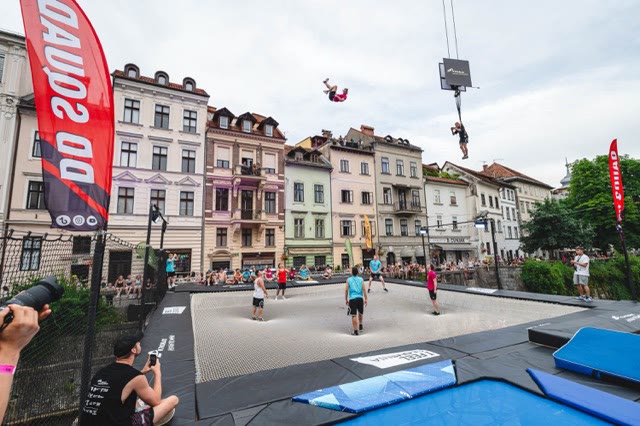 Large trampoline stage on the river in Ljubljana with spectators and two acrobats high in the air
