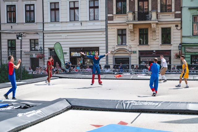 Performers in superhero costumes on the trampoline in front of spectators on a city square