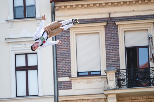 Performer in traditional costume and suspenders flipping in front of a historic building