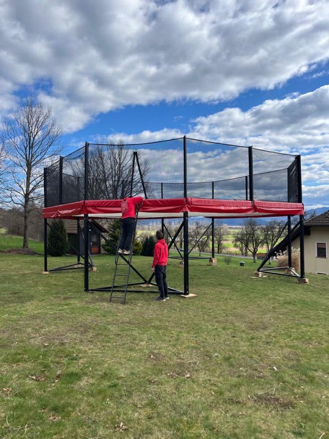 Two team members setting up the raised megatramp frame on a lawn under a cloudy blue sky