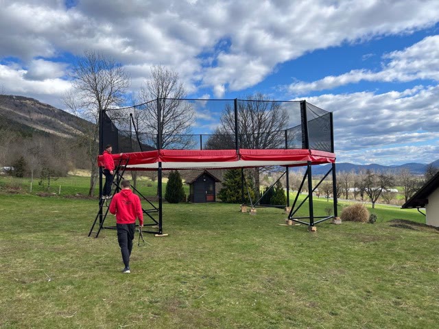 Megatramp with red padding and safety nets on a lawn in front of hills as the team prepares it
