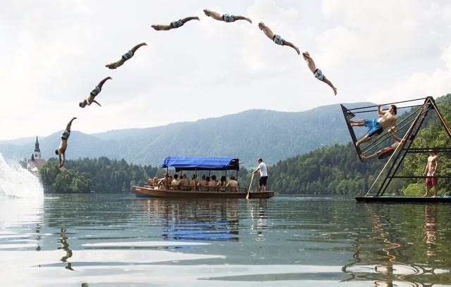 Multiple-exposure image of a diver flipping off the russian swing into a lake with a boat of spectators below