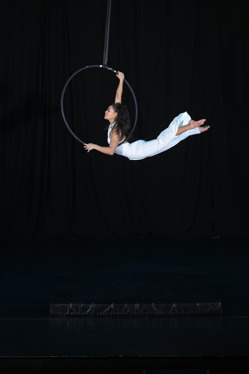 Aerialist in white flying through an aerial hoop against a black curtain