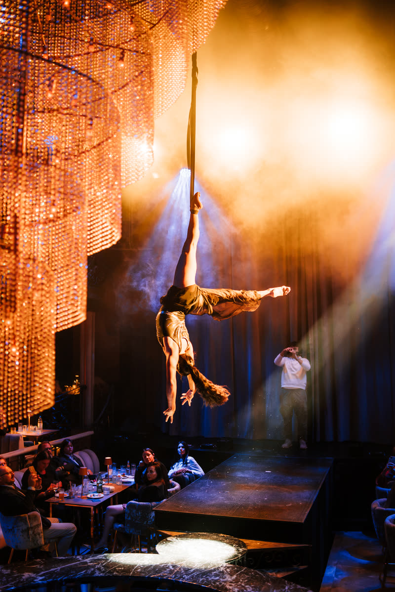 Aerialist in an upside-down split high above a banquet hall with a crystal chandelier