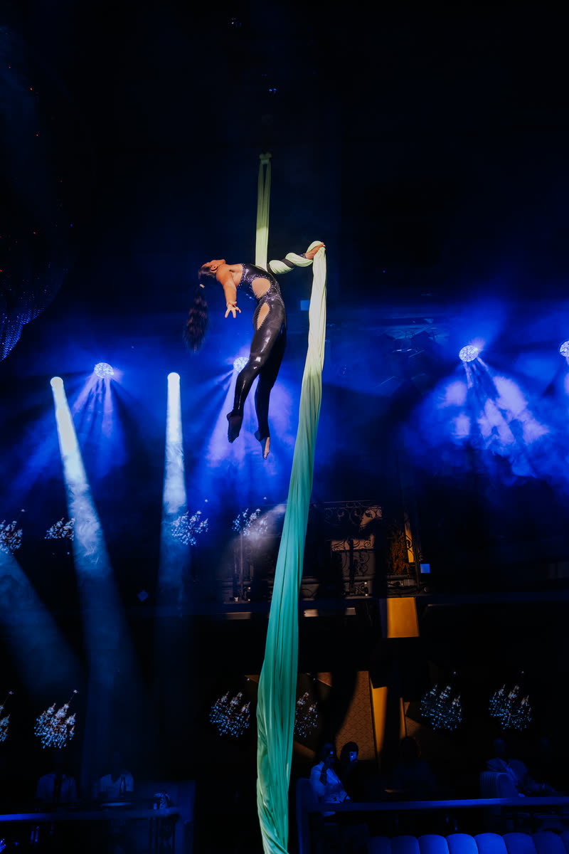 Aerialist on green aerial silks under blue spotlights