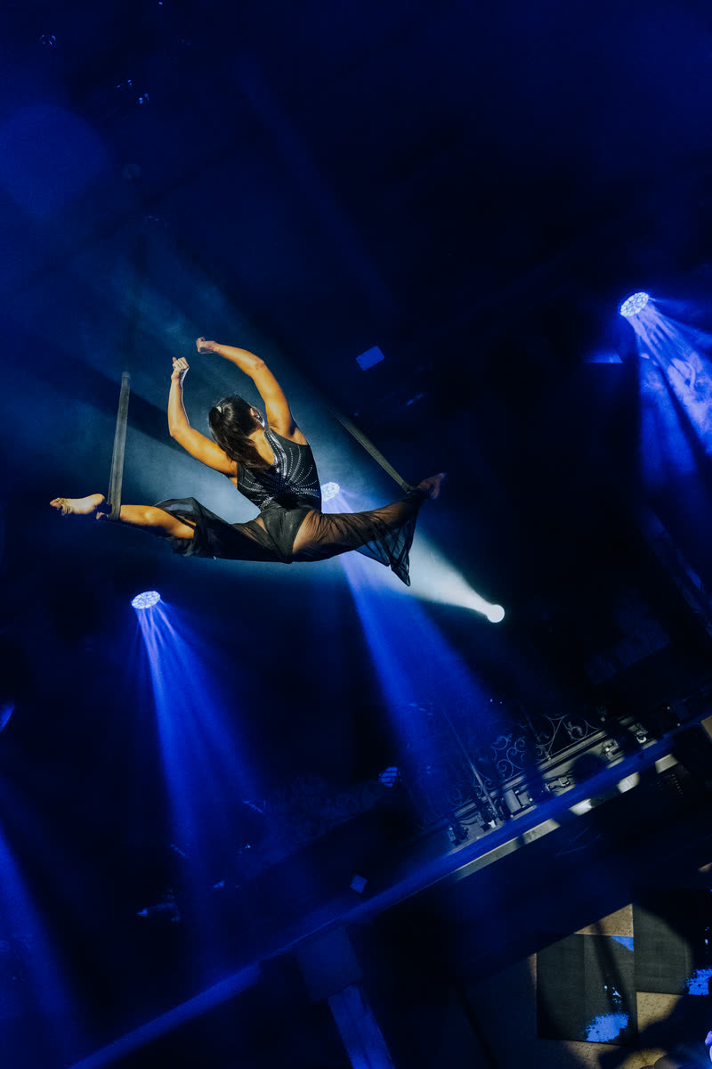 Aerialist in a dramatic mid-air pose under blue stage lights