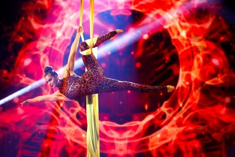 Aerialist on yellow aerial silks in front of a red graphic stage backdrop