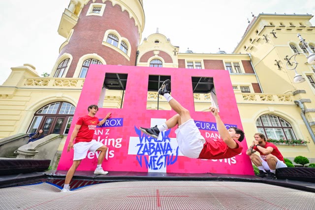 Young participant doing a flip off a pink trampoline wall in front of a historic building