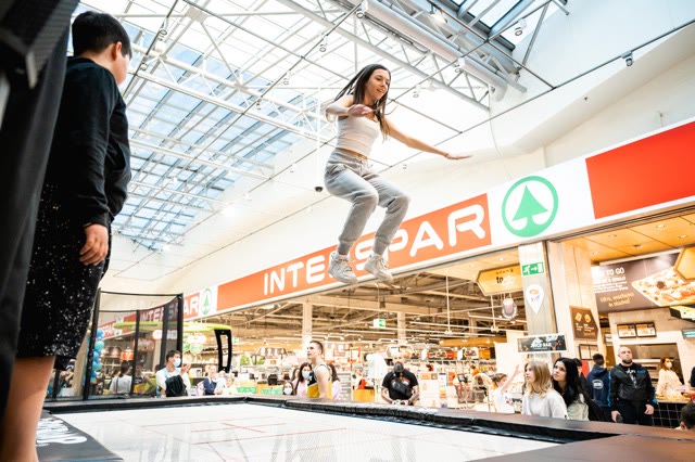 Girl jumping on a trampoline in a shopping centre while children and visitors watch