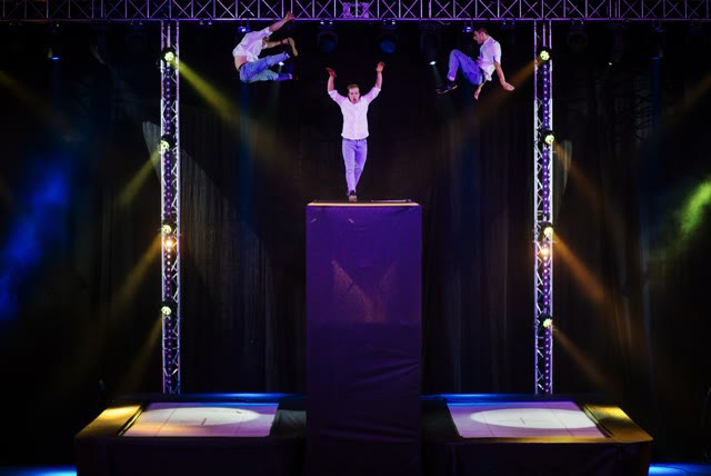 Acrobat leaping from a stage tower between two trampolines under stage lights